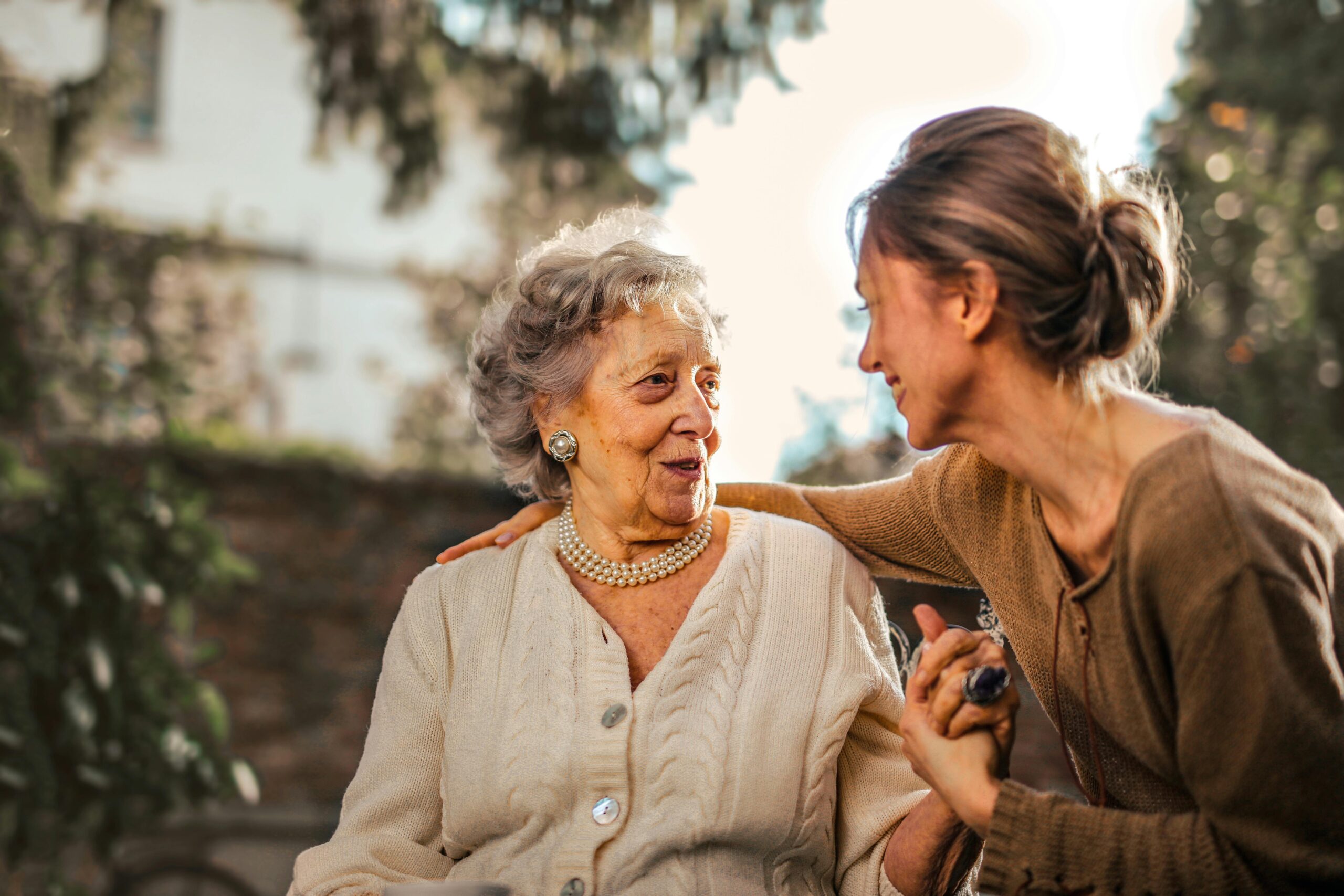 Help At Home Elderly woman and adult daughter share a joyful, affectionate moment in a sunny garden.